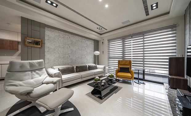 
客厅
Living Room

客厅选用屋主喜爱的灰褐洞石作电视牆，其天然纹路及不规律的凹洞，塑造独特视觉感受，并与沙发背牆的石纹壁纸相呼应，周边搭配妆饰线条的浅灰立面、灰镜，放大场域同时以和谐的色彩串联成大气样貌。

We chose silver-gray travertine, as the homeowner’s preference, to decorate the TV wall. The natural veins and diffusing pitted holes create a unique look. And then, assort with a trimmed light gray facade, appealingly echoing the marble-textured wallpaper behind the sofa. Besides, the tinted mirrors enlarged the space visually and harmonized the whole field with an extravagant quality.
