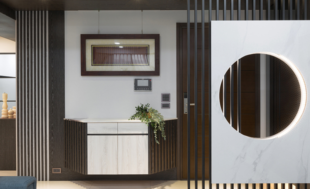 
玄关
Foyer

玄关採用木皮天花板和铁件格栅，与其他场域区隔，引导初访道友自然走至廊道转角的神桌；入门即见的圆形镂空屏风，以澹色纹理的纯白法国大理石，镶嵌灯带与木质，避免「穿堂煞」风水顾忌的同时，仍保有空间与光线的通透感，而「圆」的图像则带有团圆、圆满的期许，也符合佛教吉祥图饰，藉由简单却富含意象的设计抚慰生活与心灵。

Set the ceiling with wood veneers and erect an iron grid to separate the foyer from other areas and lead the fellow cultivators to the home Buddhist shrine at the corner. We exploit a white marble slab and hollow a circle with lighting to set a screen at the entryway that eases the geomancy taboo and keeps a transparent look at the same time. And the round shape implies the image of reunion and perfection, which conforms to the auspicious decoration of Buddhism and comforts life and soul with a simple but meaningful design.
