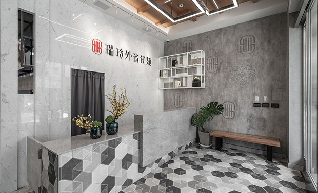 
柜檯
Front Counter

接待区铺陈復古的六角砖并向上延伸至柜檯，另叠加纹路细緻的大理石材，搭配一旁俐落的铁件层架与别具一格的造型logo牆，为延续二十多年的传统美味添入新气象，而后方的招牌背牆则选用业主锺情的卡拉拉白石材，其细腻的肌理与石质大气的质感相映成趣，旁侧特意裁切一道方形空洞，兼具减轻量体与透视之效，增添空间的层次感。

Skillfully lay the hexagonal tiles from the flooring to the facade of the front counter, which combined the exquisite marble materials, assorts with the mounted iron shelf at the side and the unique feature wall, remarkably creating a welcoming ambiance to the place for over 20 years serving. We strikingly exploit the Carrara white marble to manifest the brand logo, artfully casting the polished marble front desk. Furthermore, meticulously set a square entrance on the side that grows a concise feeling but visually rich space.
