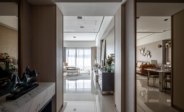 玄关
The foyer

格局狭长的玄关，天花板採挑高设计，并于两侧牆面贴茶镜，透过暗金色的镜像，充分拓展空间感，也让人一进门，便被温暖而大气的景色包裹；左侧的石纹区块，除可收纳穿鞋椅外，本身亦为艺品展示台，让此处不仅作为过道，更拥有区域自身的美感个性。

Due to the foyer of long and narrow pattern, the designer elevates the ceiling and paste tea mirrors on both sides walls, which enlarge the space via the dark golden mirrors reflection; while entering the house, people immediately receive the soft and distinguished ambiance. The marble countertop on the left side serves as an art exhibition platform, and the underneath position can place a shoe stool, as well as to create the exclusive beauty of the corridor.