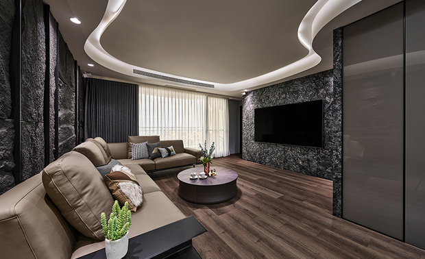 客厅
Living Room

敞朗的客厅场域，注入沉静深灰色调，带来安定稳重的效果。大片纯白天花板平衡色温，以弧线曲面延续玄关流水意象，直至餐区串连整体视觉，流通的动线使客、餐厅相容一室。天花的线性语彙，并非是为了做造型，而是依循梁柱结构，将电路管线埋藏于此。

电视牆选用金色山脉大理石材，形塑恢宏气势，沙发背牆以环保PU板，拼接山岩意象，并置入储藏室；两相呼应室外行道树，引景入室虚实相融，自然气息流淌而至。除了立面採用绿建材，在天花板的工法上，亦透过数位CNC切割方式，减少现场废弃物及施工时间，大幅降低对环境的负担。

The spacious living room exuded a reposeful vibe in a dark gray scheme. A large area of clear white ceiling harmonized with the color palette, and its curved shape extended the streaming image from the entryway to the dining area. In addition, the living room coordinated with the dining room by following the ceiling outline. The patterned ceiling design helped organize and hide the wiring and beams; it surprisingly presented an elegant accent.  

Brazilian black granite TV wall cladding contributed a grand style. Then, we built a storage room behind the sofa background wall, and the facade was installed with Eco-friendly decorative PU stonewall panels. The rocky embellishment performed a natural view integrating the outdoor greenery. Besides using Eco-friendly construction materials for the room facade, we also adopted a CNC machinery system that can reduce wastage and working time. We try our best to decrease Eco-consumption.

