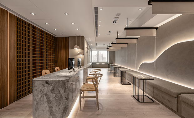 
本文由OPEN编辑部撰写

设计概念 Design Concept

沿循斑驳纹理的曲弧壁面转入门中，映入眼帘的点点绿植为空间灌注盎然生机，而漫佈壁面的和煦光晕向内蔓延，点亮由温润木韵及细腻石材拼筑成的朴实长廊，与廊道尽头的明亮日光相迎、交融，齐组清新柔和的舒心环境。

呼应企业商标的圆润造型、以及提供女性客群为主的医美服务，简兆芝室内设计 简兆芝 主持设计师 于多处立面、天壁汇入流线、圆弧设计，象徵女子优雅的身体曲线，并将业者「以人工美呈现自然美」的理念作为设计核心，藉由同是人为的室内装修展现天成美感，全案铺叙木质、大理石与彷溷凝土质感的特殊涂料，辅以入口旁植栽区、走廊末端引入的天光，挹来置身户外般的纯淨自然气息，间或点缀布艺、镀钛铁件等人造材质，堆迭细处层次感同时，完美呈递融汇品牌概念的医疗场所。

Walk along the rustic textured wall and turn by the curved corner, and you may see refreshing greenery bringing an organic feel into the space. Pleasant lighting spills upon the walls and glows the pristine corridor with a warm wood tone and delicate marble. The clear, soft style contributes to a calming accommodation, inviting bright sunshine from the end.

The clinic provides aesthetic medicine services to female target clients, echoing the brand image by the logo in a round shape. INK DESIGN SPACE's presiding designer Kathy Chien adopted curves and rounded shapes to signify elegant women's body shapes. Besides, they developed the design based on the clinic's brand concept- “artificial beauty complements natural beauty.” Similarly, the interior decorations contribute to shaping a natural character. The project incorporates natural materials such as timber, marble, and concrete textures made from decorative paint coordinated with artificial fabric and metallic elements, adjoined green plants, and natural light. Exquisitely, comprehensive layering approaches reveal a perfect branding medical practice.

设计手法 Design Techniques

细划场域 顾及隐私
Meticulous Floor Plans Preserve Privacy

考量医学空间对机能的讲究，设计师依各区功能划分前、中、后场；前场的接待候诊区为公共区域，透过于座位间悬挂可自由垂下的拉帘，予以顾客们具隐私的等待场所，而中场的问诊区作为衔接前后两区的中介空间，藉由设置于窗畔转角的入口、柜檯后方的出口，独立访客进离场的路径，确保后场的诊疗室及术后休息区宁静私密之馀，打造出流畅无碍的动线。

Concerning the facilitation of medical care, the designer planned three sections based on functional requirements. The front section is a public space, including reception and waiting areas. In the waiting area, curtains between the seats provide privacy for the clients. The consultation and examination rooms in the middle serve as a linking section, forming an exclusive, unimpeded flow. The layout of entering from the door beside the window and leaving by the door behind the reception counter ensures the tranquility and privacy of the rear treatment and recovery rooms.

匠心独运 环保健康
Inventive Ideas & Eco-friendly Manners

候诊区前方採用表面涂刷特殊漆的磁性牆，搭配上方磁石材质的字体，使业者未来变更标语时能轻鬆更动字母位置，避免拆字补漆造成的多馀耗材，另于注重卫生安全的手术房、实验室等处施作设计团队研发的环保建材，大幅降低VOC和病菌的孳生，成就友善健康的无毒环境。

A magnetic wall lined with decorative paint in the waiting area allows different slogans to be displayed, avoiding additional work and waste. Besides, eco-friendly building materials developed by the design team are adopted in the sanitized operation room and laboratory, eliminating VOCs and bacteria growth. As a result, they accomplished a healthy and non-toxic space.

全面服务 完善所需
Considering Services & Perfect Satisfaction

思及医疗商空缜密漫长的开业程序，设计师细腻控管时间排程，同时进行多项设计专案及工程执行，令业者取得执照后得以迅速开张，缩短承租空间后无法营业的空白期，自多元面向提升室设服务品质。此外，本案配置大量间接照明搭配质朴自然材质，不仅赋予人们归宅般的温馨放鬆感，也实现来访者皆能自在无压的业主期许。

Regarding the long-term and complicated procedures for opening practice, the designer shortened the construction duration by managing various works and projects in the meantime. It is an effective service that favors rental abatement under construction. Additionally, sizeable indirect lighting matches pristine textured materials, rendering a balmy and homelike feel to the clients. All visitors can relish in the unstrained atmosphere the business owner aspires to.

