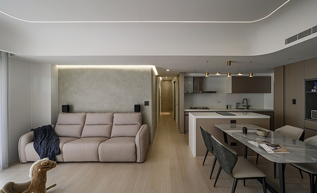 本文由OPEN编辑部撰写

设计概念 Design Concept

夜晚，身披倦意徐步返家，甫入玄关，和暖木韵轻柔包裹全身，予人沉静疗癒之感，步至厅堂，周围环绕的轻浅色调无形舒缓身心，暖黄照明酝酿属于「家」的放鬆氛围，伴随一声温柔的招呼，温馨暖意满盈心中，竟日繁忙的疲惫也随之消散无踪。

回应屋主对敞亮空间的嚮往，棠禾设计 曾智和 设计总监 划设流畅单纯的动线搭配开放式公领域，令户外自然光可照亮公区各隅，并减少使用嵌灯，改以线灯、间接灯光作为主要照明，营造柔和舒心的自适感受，配合业主锺情的澹色基底及软装，成就明亮开阔的休閒场所。

As the night falls, the homeowner returns home, suffering from fatigue. Balmy wood texture embraces and comforts him as soon as the door opens. The interior light-shaded surroundings soothe the mind and soul, and the warm yellow lights bring about a homey relaxation. A sweet greeting casts the all-day tiredness and lovingly melts his heart.

To implement the homeowner's vision, Tang He Design's design director TSENG CHIH HE arranges an airy space by curating smooth moving flows in an open floor plan. The brilliant layout invites natural light into each corner of the public domains. Rather than cove lighting, we take linear and indirect lighting as the primary illumination, and the lighting design benefits elegant and relaxing feels. With the homeowner's favorite neutral palettes, soft-colored furnishing and backgrounds effectively shape a delightful living space.

设计手法 Design Techniques

现代时尚 简洁不失暖意
Minimalist and Balmy Trendy Charm

本案于客、餐厅天壁及多处转角汇入弧形元素，佐搭立面洗练线条，为空间挹注优雅而俐落的时髦风韵，且于公领域选用光洁的水磨石电视牆，塑造一方素淨清爽的明朗景緻，辅以暖色家具、柜体和象徵品牌的木纹元素，赋予居者温润舒适的生活环境。

Coordinated with sleek walls, we implement multiple curved elements to the corners and dining room ceiling, revealing a nifty and trendy approach to the project. A distinguishing glossy terrazzo TV wall contributes a clean and bright look in the public space. Aligned with our brand identity, we adopted furniture in warm tones and achieved a balmy and comfortable living environment.

丰富机能 贴合业主所需
Satisfying functionalities Meet Exclusive Demands

考量业主偏好简餐的饮食习惯，餐厨区设置一座搭载IH炉的中岛，方便使用者製作轻食，其下方立面结合收纳功能，提升取放厨具、碗盘的便利性，此外，电视牆旁规划一座半开放柜体，供住者展示、收藏喜爱的模型和球鞋，对侧餐边柜则藏入通往后阳台的暗门，内部畸零地划为储藏室，充分满足储纳打扫用具和日常用品的需求。

Considering the homeowners' cooking preferences, we arranged a kitchen island with an induction cooktop for light meal preparation. Meanwhile, the kitchen island incorporates tableware storage underneath. In addition, an open shelving design next to the TV wall showcases model figures and sneaker collections. On the opposite end, we installed a hidden door to the back balcony and took an odd space as a storage room for keeping daily supplies and cleaning utensils.

居家安全 造就幸福未来
Safe Dwelling Contributes Future Happiness

思及屋主家中育有一名学龄前幼童，开放式场域利于夫妻二人随时注意幼子活动安全，而公领域选用圆角餐桌和软质餐椅取代茶几、边柜等小型家具，降低孩童碰撞危险性，另于全案採用无甲醛的系统柜及艺术涂料，搭配耐用无毒的塑合板材，共筑健康环保的理想居所。

Exclusively, we arrange an open floor plan that allows the homeowner couple to be concerned about their preschool child's safety at times. Instead of small-sized furniture, such as coffee tables or low cabinets, we selected a rounded-edged dining table and tufted chairs to prevent bumping. In addition, the entire project is applied with non-formaldehyde built-in furniture, decorative wall coating, and nontoxic plywood panels. With the use of Eco-friendly building materials, it is an ideal and healthy dwelling environment.

