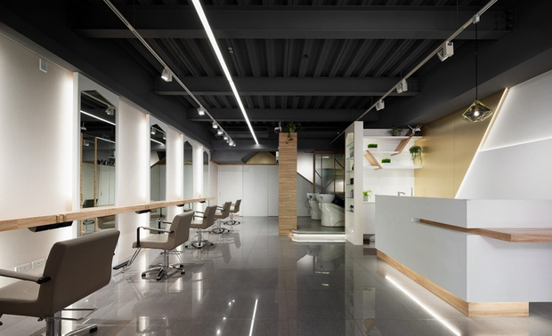 本文由OPEN编辑部撰写

设计概念 Design Concept

本案为新成屋楼中楼商空，巨设计集团–GD回应业主期望，以最低代价及拆更最小范围，满足美髮沙龙的需求及视觉变化的多样性，展现品牌专业度和对环境的关怀。

经营者将年轻人、家庭和关注时尚的人们定为本案主要客群，期许以现代、俐落、乾淨的质感商空吸引顾客，因此设计师设定几何中的「斜角」为主轴，搭配白色、木纹和流线灯光构筑场域，并依照服务流程规划区域及配置灯具、善用梯下畸零地设置收纳柜，打造员工、访客皆便利舒适的空间

沿简约素雅入口造型牆，推门入内，天壁的笔直条灯串连入口至楼梯，镜面和抛光砖反射线灯及大小各异的斜角造型，将色块、光线、典雅灯具……一化为多、无限延展，缀点出简单而富有层次的美髮沙龙。

In response to the new-build business duplex, D.G.d International Design conducted the least-cost renovation and achieved what a hair salon demands, with various transforming visions. The project distinctively reveals the professional brand and eco-friendly approaches. 

The business operator targets youngsters, families, and people who care about fashion trends as their significant customers. They aspire to invite customers with a modern and sophisticated business space. Therefore, the designer adopted diagonal elements to match white and wood tones, staging the interior beneath the linear lighting. Besides, each area facilitates different service processes with various lighting fixtures, while under-stair storage contributes to an easy and convenient space for the staff and customers.

Characteristic designs lay from the entrance and along the sleek accent wall. Linear ceiling lighting slimly streams from the door to the stairs. Mirrors and gloss tiles make reflective diagonal images in various sizes against the slim light. The interior comprehensively organizes color blocks, illumination, and reflective sheen, presenting a minimalist and layering hair salon.

设计手法 Design Techniques

斜角镜射层次 实用选材
Reflection Layering & Functional Materials

本案以素淨纯白与暖意木质为基调，将斜角、斜线元素融入色块、灯光、美髮镜框和柜体造型等处，偕同盏盏灿金吊灯、壁灯，与髮廊中的镜面和抛光地坪共组万花筒般的视觉感受，让简约装饰达到最多变的效果，同时，壁面选用易养护的喷漆和壁纸，利于员工每日整理环境，兼顾美观及实用性。

The pure white color shade and warm wood tone work as the keynote of the project. Golden light fixtures coordinate with mirrors and glossy flooring to create a kaleidoscope vision, using diagonal elements combined with color blocks, lighting curations, mirrors, and cabinet shapes. It is perfect for maximizing transforming effects from minimalist adornments. Meanwhile, adopting easy-maintained wallpapers and covering makes the space aesthetic and functional. The versatile wall finishes allow the staff to manage daily cleansing in a breeze.

需求打光 精准检视髮型
Sufficient Illumination Enhances Viewing Hairdos

考量剪髮需要充足光线，工作区运用条灯、镜后的间接照明与可依客人座位调整位置的轨道灯，创造明亮作业环境，并顾及观看髮质、头髮造型所需，善加溷用黄白两色灯光，营造太阳光色的光源，以便顾客和髮型师准确检视不同髮型、色泽。

Considering the styling area requires adequate light for services, we strategically installed linear lights, indirect lighting behind mirrors, and adjustable track light fixtures to set up a brilliant workspace, allowing the staff to check hair conditions. Moreover, the balance of white and yellow lights creates a natural sunlight shade, enhancing the viewing experience for stylists and customers of various hairdos and luster.

轻度装修 巧排区域功能
Minimum Refurbishments & Nifty Area Functions

全案使用绿建材，且保留原有天花板和地面，仅因应洗头区的排水系统架高地坪，减少繁复装修耗费的资源，另基于业主将二楼设定为给整个家庭使用的VIP空间，善用原建筑窗边高低差形成之平台，规划供小朋友嬉戏等候的区域，让美髮中的家长也能随时看顾。

The project is applied with green building materials and complied with a minimum refurbishment. It economizes as much as possible by conserving the existing ceiling and flooring except elevating the wash area floor to adapt the drainage system. In addition, we exclusively designated the second floor for customers accompanied by family, and the window seat aligned with the widow height provides a play zone for young children as they are waiting. The thoughtful arrangement considerately satisfies the parent-customers taking care of their children.