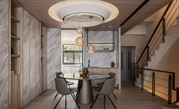 
餐厅
Dining Room

餐厅选用木作天花板营造温润舒适的氛围，其质朴纹理与壁柜的大理石纹相呼应，共同呈现山岚间的自然之美，另设计如倒置山峰的白色圆弧灯座，搭配线条简约的精緻球型吊灯，添加一抹时尚气息，一旁厨房入口规划附有水槽的吧台，方便居者享用饮品与洗涤杯器，未来养育孩童则可放置热水瓶、奶瓶消毒锅等器具，提升育儿便利性。

The wood ceiling presents a warm texture to the space and echoes with the built-in cabinets' marble veins, delivering a marvelous natural scene. Besides, the convex rounded ceiling design with simple stringed pendant lights with delicate spheres complements a modern approach. Aside from the kitchen entrance, the wet bar facilitates serving drinks or cleaning. The countertop applied a place for a water boiler or a baby bottle sterilizer required by future nursery requirements.
