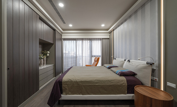 
主卧、更衣间
Master Bedroom Ensuite

私领域铺设超耐磨木地板，搭配深色调及鹅黄光源，营造沉稳温暖的空间氛围；考量屋主的过敏体质，主卧的木作床头牆以线条壁纸取代常见的床头裱布，并配合其睡前阅读的习惯，于床头两侧设置可调式的壁灯，打造自在舒适的休憩空间。

In the private space, we finished it with laminated wood flooring. The dark-shaded elements are integrated with yellow light to bring a tranquil and balmy atmosphere. Considering the allergic constitution of the homeowner, we substitute the model-upholstered headboard with striped wallpapers. Moreover, set two adjustable lamps on both sides to provide sufficient illumination for bedside reading and devise a warm and restful space.
