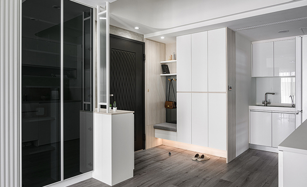 
玄关、餐厨
Entryway & Eat-In Kitchen

玄关设计一面长虹玻璃小屏风，化解穿堂煞的风水疑虑，对侧设置嵌入穿鞋椅的鞋柜，其下方的悬空设计配合柜底通风孔，保持柜内乾爽透气。

In the entryway, a slender reeded glass partition serves as a Feng Shui-friendly solution to dispel concerns about negative energy flow. Then, we deliberately set out an embedded shoe bench with the shoe cabinet on the opposite side. The suspended design and ventilation holes at the bottom ensure a dry cabinet with good air circulation.
