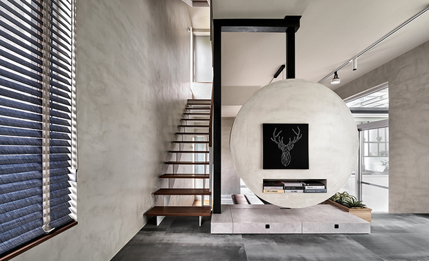 
客厅
Living Room

与餐厅的水波纹大理石餐桌遥相呼应，客厅选用带有水墨感的挂画与圆地毯，配上一座色彩活泼亮眼的蓝绿色弧形沙发，让家人共处时更具凝聚感；对面的电视牆突破制式的方形样式，以铁件悬吊圆形量体，犹如復古钟摆的造型，在方正空间中是独一无二的视觉焦点，且带有家庭圆满的象徵意义。

The ripple marble dining table in the dining area perfectly works in concert with the design theme in the living room, where ink-inspired artworks and a circular rug set the stage. Besides, we complemented a vibrant blue-green curved sofa to foster a stronger sense of togetherness among family members during their shared moments. Across from this inviting space, the TV wall breaks free from conventional rectangular patterns. Instead, it features a suspended circular structure made of iron, resembling the look of a vintage pendulum clock. In the midst of a rectangular room, it stands as a unique visual focal point, symbolizing the completeness of the family unit.
