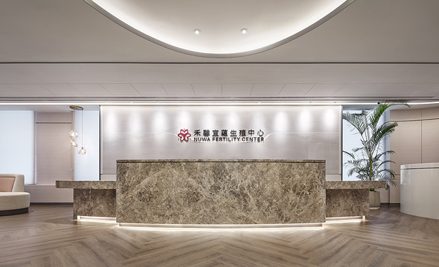 本文由OPEN编辑部撰写

设计概念 Design Concept

心怀孵育雏鸟破壳的希冀，无数期盼的父母携手专业医疗人员，以深厚的爱与精密科学技术，于生殖中心搭筑起温暖坚实的巢，尽心照护新育胚胎，共同守望新生命降临的瞬间。

简兆芝室内设计 简兆芝 主持设计师 由「女性怀孕的身体姿态」汲取灵感，结合自然界孕育生命的蛋之意象，令饱满曲弧包覆天壁及立面，如同张开双臂迎接每位访者，又似母亲怀抱新生儿的温柔，伴随无甲醛的F0板材，质感柔和的木质、壁布，打造居家般舒适的医疗场所，抚慰就诊者内心的焦虑，传递沉稳可靠的品牌精神。

With the evocation of a bird hatching from the egg, numerous parents-to-be take advantage of medical professionals' support and fertility technology, lightheartedly nesting precious offspring. In the fertility center, everyone is dedicated to caring for embryos and inviting new lives with all hearts.

Innovatively inspired by a pregnant mother figure, INK DESIGN SPACE's presiding designer Kathy Chien integrated the appearance of an egg that implies a birth in nature. Bulbous rounded ceilings and surfaces greet visitors with a warm embrace. Additionally, zero-formaldehyde F0-certified wood panels and soft-textured wall fabrics perform a homey space as gentle cuddling that comforts the client's anxiety. Therefore, these delicate approaches deliver a stable brand spirit.

设计手法 Design Techniques

温馨时尚 传递品牌信念
Warm And Trendy Style Establishes The Brand Identity

秉持「医疗场域应令人安心信赖」的念想，全案以中性的米灰色调为主，搭配柔和的木质地坪与曲弧元素，洋溢温暖自在的气息，辅以精緻的镀钛金属、皮革和灯具缀点，增添画面层次，并置入粉紫色系的弧形软装，呼应核心意象，而融入其中的商标色彩，不仅串连起集团旗下分店，更奠定出鲜明的品牌主视觉，令消费者留下深刻印象。

The project accentuates ''a trustworthy medical institution'' mission. In the neutral pallets, elegant wood flooring and curved elements positively present a balmy vibe. Sophisticated materials like titanium-plated iron, leather, and lighting fixtures feature layering approaches. In addition, as the logo color, curved pinkish purple furnishings echo the primary concept and set a distinctive brand vision identity for the entire medical group.

巧划动线 控管隐私风险
Ingenious Smooth Flows & Exclusive Privacy Control

案场依循就诊者和医疗人员的身份划设动线，之于前者，每个诊间都设有内诊间，看诊时不需往返不同空间，另将更衣间设于通往手术室的途中，避免手术衣暴露在公共区域，降低感染风险，后者则依循另一路径，先经过空气浴尘室消毒全身，再由第二入口进入手术间，让两者仅在一处交会，兼顾双方隐私。

We strategically create exclusive traffic flows for medical professionals and clients separately. Each consultation office incorporates an exam room that facilitates the clients. Besides, we allocated the staff changing room on the way to the operating room. The considerate layout prevents sterile surgical gowns from being exposed to public areas and eliminates infection risks. On the other hand, the clients have to go through an air shower chamber and enter the operating room by the secondary door. As a result, the medical professionals and the clients can only meet at the specific spot with privacy.

多样工法 细緻关怀生命
Various Solutions Preserve New Lives

思及新育胚胎十分脆弱，全案皆採无甲醛材料，并使用专门除虫剂杜绝可能附着其中的蠹虫卵，打造最安全纯淨的培育环境，此外，板材表面服贴特殊材质，避免场所每日的消毒作业减损建材寿命，建构易维护的无毒场域，成为医疗人员们最可靠的后盾。

To create a clean and safe environment for vulnerable embryos, we adopted zero-formaldehyde building materials and exploited specialized wood treatment to prevent pest infestation. Besides, the project finishes with sterilizing sustainable surfaces that cope with the infection control process. An easy-maintained and healthy interior design offers full support to all medical staff.
