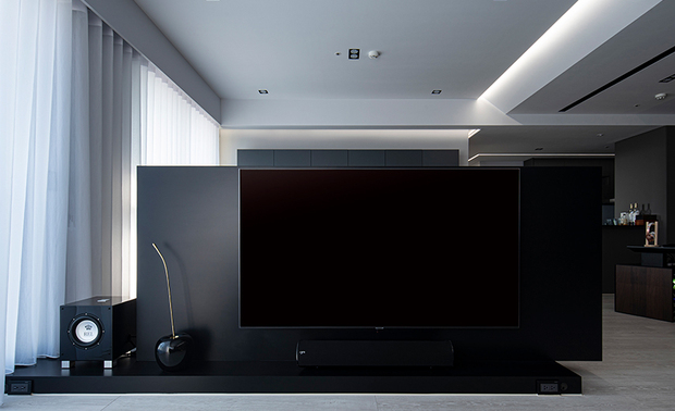 
客厅
The living room

客厅浅灰色的木作沙发背牆，透过内嵌式的远红外线控制系统，将电器设备皆藏入后方储藏室，使对面的深黑烤漆电视牆，保有整洁外观，配上檯面、立面错置拼接的造型，展现俐落的层次美感。

The storage room behind the light-gray wooden wall at the rear of the sofa ingeniously conceals the audio-visual equipment, which operates via the embedded far-infrared control system; thereupon, to keep the opposite dark-black baking varnish TV wall a neat look. In addition, the staggered arrangement of the TV stand and the TV wall shows the beauty of smooth layers.
