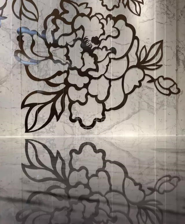 在一层的内厅区域，一面玫瑰花纹样的造型墙格外抢眼。而这看似平面纹样的背后，竟然是层层的石材与镭射切割的金属拼贴而成。
每块石材的宽度不一样，每块石材背后的石材数量也不一样。而镭射切割的花纹，也被切割成与石材匹配的宽度。
