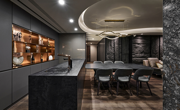 餐厅
Dining Room
餐厅动线以中岛及餐桌,建构T字型动线,视觉直面主牆,以酒吧概念,打造餐酒馆氛围,并兼具收纳与展示效用。柜体上方置入100吋的声控投影幕,与客厅电视同步,享受观影或看球赛的舒适体验。中岛右侧立面则设计为烤漆玻璃牆,供会议时纪录书写用。通往私领域的廊道,延续客厅沙发背牆视觉,以层迭拼接的方式,内嵌感应灯源,信步于此,光带逐一显现,达到渐层效果,凸显明暗层次。
First, we planned a T-patterned circulation around the dining table and the counter. Bringing a bistro vibe to the space, the focal point accentuated at the showcase cabinet incorporated storage and display. Next, we installed a 100-inch voice control ceiling recessed projector screen above the cabinet. The homeowners can enjoy a movie or a sports game on the large screen synchronized with the TV in the living room. Third, the lacquered glass wall mounted on the neighboring counter served as a writing board during meetings. Finally, install motion sensor lights along the hallway to the private domains so that the brightness would occur gradually with each step and create a gradation of light and shadow.