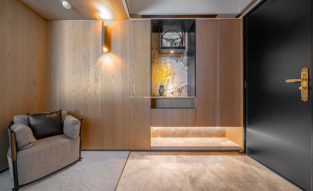 
玄关
Entryway

玄关以金属穹顶做为家的开场，接续立面及地坪石材，喻示不凡气质与磅礴气场。大面木质柜体由此延续至公私领域，奠定家屋温润气息，透过不同灯光配置，呈显纹理表情变化，于收纳同时亦带展示效果。为因应一家五口大量储物需求，我们在左侧划设储藏室，採用真皮立面结合镀钛框线收边，流露优雅设计语彙，平时外出鞋履衣物、球具及行李箱，都能收束于此。而针对不同家庭成员的身高和需求，也为其规划了固定高度与可弹性移动的穿鞋椅，让外出或进门穿脱衣物，都能从容且舒适。

The stone façade and flooring signify an imposing and dignified flair at the entrance, starting with the gloss-trimmed tray ceiling design. The whole wall cabinetry, equipped with a storage system, expands a balmy touch to the entire area and features wood grains. On the left, a leather-paneled door outlined with titanium-plated trims presents an elegant language; sports gear, suitcases, coats, and shoes belonging to the five family members are well organized behind it. Besides, the adjustable and movable shoe bench serves comfortable and convenient seating for residents of different heights.
