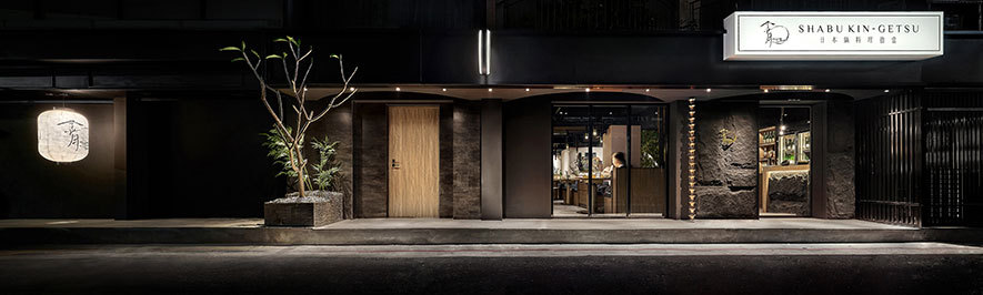 本文由OPEN编辑部撰写
设计概念 Design Concept
静矗于栉比高楼间,一幢披着深色石皮的玄色平屋几与夜色相融,簷下悬挂的灯笼随着晚风款款摇曳,流泻月光般朦胧光晕,引人步趋探寻。轻启门扉,一阵锅香窜入鼻尖,旋即映入眼帘的「金月」二字与蓝白纸笼发散幽然微光,相伴石、竹交织的半弧端牆和枝叶隐现的高耸碧竹,彷彿落入悠远的江户时期,浓厚的日式古韵使每位访客留下深刻印象。循迳入内,宛若月形般圆弧相接的座椅整齐罗列,人们于其间共享传统锅物与新鲜物产,在味蕾与视觉的飨宴中,享受如望月般圆满的团聚时刻。
发想自品牌「金月」之「月」字,简兆芝室内设计 简兆芝 主持设计师 以「月圆」的形象为主轴,从店面主视觉牆、客席区卡式座椅、锅物餐具等皆融入「圆」的形貌,将其圆满、团圆的美好寓意传达予每位顾客,同时回应高端日式锅物店的定位,运用原石、石皮、木皮、金属等现代建材,结合日本竹子与传统灯笼,表现古今交融的和风禅韵,并于其中体现我们积极找寻各式平衡的理念,透过和谐的设计手法与讲究自然的料理彼此相衬,建构食材与空间对话的桥樑,进而筑起用餐者与料理者的共鸣,达成场、人、食三者平衡圆满的状态。
Standing gracefully amidst towering buildings, a one-story jet-black house clad in deep-colored stone veneers harmoniously blends with the night. Lanterns hanging under the eaves sway gently in the evening breeze, casting a soft halo akin to moonlight, inviting curious souls to explore further. As the door opens, the delightful aroma of cooking wafts into the air. The sight of the Chinese characters of Golden Moon and the blue-white paper lanterns radiate a subtle glow, accompanied by the interwoven stone and bamboo curved end-wall and the tall emerald bamboo revealing its branches and leaves. It feels as if one has stepped back into the distant Edo period, leaving a profound and memorable impression on every guest with its rich Japanese antique charm. Upon entering, neatly arranged seating in the shape of a crescent moon welcomes guests, where they come together to indulge in a typical hot pot, fresh vegetables, and meat. The guests enjoy moments of reunions, complete and fulfilling, akin to the sight of a full moon, with an unparalleled feast that delights their senses and tantalizes their taste buds.
Inspired by the Moon word in the brand Golden Moon, INK DESIGN SPACE's presiding designer Kathy Chien centered her design on the image of a Full Moon. Incorporating the concept of Roundness, we skillfully infuse the theme of a Full Moon throughout the feature wall, the booth-style seating area, and the tableware for hot pot dishes. By integrating the symbolism of completeness and togetherness that the full moon represents, we aim to convey a sense of joy and harmony to every guest. Our design caters to the positioning of a high-end Japanese hot pot restaurant. We artfully exploit modern building materials, such as natural stones, stone veneers, wood veneers, and metals, combined with traditional Japanese bamboo and lanterns to evoke a blend of ancient and modern Japanese Zen aesthetics. Moreover, we actively embed the concept of seeking various forms of balance, performing a design that agreeably complements nature-inspired cuisine. By establishing a dialogue between the ingredients and the space, we create a bridge for interaction between diners and culinary creations, achieving a balanced and harmonious state among the ambiance, the people, and the food.
设计手法 Design Techniques
风格主牆 镌刻品牌
Impressive Feature Wall: Carving the Brand Identity
配合店面形象的展现,我们于入口处设计一道主视觉牆,藉由天然的石材与竹子彰显质朴踏实的日式精神,并悬挂数盏象徵圆满意象的灯笼,其印有虎、兔图案,隐诉餐厅于虎年筹备、兔年呈现的品牌故事,而蓝白双色则在日本文化中具有喜气的含义,运用饱含寓意的吉祥物件、自然建材,打造和风感浓厚的特色门面,令顾客印象深刻。
In harmony with the store's identity, we meticulously set out a feature wall at the entrance, showcasing the essence of Japanese simplicity and authenticity through natural stones and bamboo. Several lanterns, symbolizing completeness and harmony, are hung on the wall, featuring motifs of the tiger and rabbit, which convey the brand's story related to the preparations during the Year of the Tiger and the unveiling during the Year of the Rabbit. The blue-white color palettes carry auspicious meanings in Japanese culture. And via exploiting these meaningful elements and natural building materials, we marvelously create a distinct and striking traditional Japanese facade, leaving a lasting impression on guests.
圆月流溢 一气呵成
Seamless Integration: Enchanting Lunar Harmony
此案以代表满月的「圆」为主题,除了入门的弧形主牆、球形灯笼,也将月的阴晴圆缺表现于客席区,设计出半圆形卡式座椅与曲弧边角的餐桌,配合订製的圆弧器皿、食器,令空间至料理一体连串,带给顾客别緻的用餐体验。
Inspired by the full moon, this overall design revolves around the theme of Roundness. Embracing the symbolism of completeness and togetherness, we strategically integrate the representation of the moon's phases throughout the restaurant. From the graceful curved feature wall at the entrance to the spherical lanterns, we cleverly presented the essence of the moon. In addition, we delicately design semi-circular booth-style seating and tables with rounded edges in the dining area, evoking the lunar motif. Bespoke arc-shaped cutlery and tableware further enhance the connection between the space and the culinary delights, providing customers with an exceptional and captivating dining journey.
细腻佈局 无拘享食
Exquisite Arrangement: Relaxed Dining Pleasure
回应业主为客人营造舒适用餐环境的坚持,客席区的半圆形卡式座椅兼具包覆感与区隔性,予以顾客安心自在的餐叙空间,另规划一间独立VIP室和两间可合併为一的多功能包厢,内设独立盥洗室,便于多人聚餐并保有良好隐私。
In response to the proprietor's unwavering commitment to creating a cozy and inviting dining environment for guests, the semi-circular booth-style seating in the dining area offers a perfect blend of coziness and privacy, providing guests with a comfortable and enjoyable dining experience. Additionally, we carefully set up a separate VIP room and two versatile private dining rooms that can be combined into one. Each room is equipped with a private restroom, allowing group gatherings while ensuring excellent privacy.