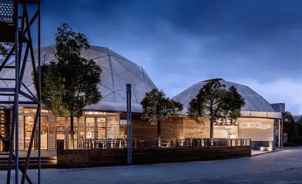 明日世界设计中心，是上海世博会时留下来的临时建筑，这些年里，也换了好几个业主，他们对建筑物的室内都进行过不同程度的改造，所以最终留下来的内部结构相对比较复杂。
在多次结构改造过程后，原有的结构框架已变得十分混乱，但没想到，这无意的混乱，却天然地透着一种能瞬间打动人的力度和美感。
另外，原有的建筑是单层膜结构，整个室内的能源损耗会很大，为了节省能源，同时，又能将现场球形网架的气势和裸露结构的美感保留下来，我们跟材料公司协商后，在室内加多了一层透明膜。
通过膜结构，自然光会照进整个室内，那么在主色调上，我们就选用了比较浅的灰白色和原木色组合，这样第一感觉很轻松，也很符合空间的多变性，例如，在举办活动或者展示家具时会经常改变平面布置，干净柔和的浅色调就可以让它变得更容易实现。