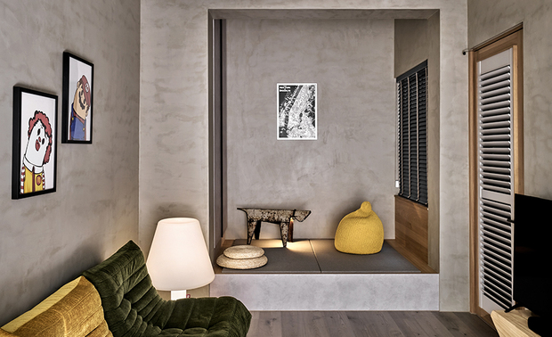 
多功能室、庭院
Multifunctional Room& Courtyard

多功能室的软装选配精緻而復古，并带有特殊配色与轻工业风，契合业主身为怀旧动画师的品味；入口右侧则特别架高一处舖设榻榻米，搭配高度合宜的天花板设计，为兼具小憩、储物与客房功能卧榻区，打造出将生活框景的视觉效果。落地窗外的庭院，以大型植栽为前景，楼梯绕道为背景，加上百叶窗引入的自然天光，由内而外叠加景緻，呈现简雅而带有层次感的寂静画面。

The interior setting in the multifunctional room are carefully curated with a touch of vintage charm and unique color palettes, perfectly aligning with the homeowner's taste as an animator. On the right side of the entrance, a raised platform with tatami flooring and a well-designed ceiling provides a multifunctional space that serves as a cozy nook, storage area, and guest room, brilliantly creating a stunning focal point in the living area. Outside the floor-to-ceiling windows, a courtyard with large plants in the foreground, stairways winding in the background, and the natural daylight filtering through the blinds all come together to create an elegant and layered view, presenting a serene and picturesque setting from the inside out.
