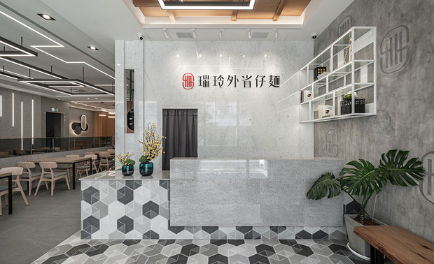 
本文由OPEN编辑部撰写

设计概念Design Concept

宁静的街区中，一幢简约纯白的建筑在暖阳的烘托下，绽放清新明亮的朝气，也凸显外牆上一抹鲜红的招牌色彩，徐步入内，印入眼帘的相异灰阶铺展质感满盈的现代风范，传承近半甲子的浓郁麵香飘荡其中，呈予饕客创新与怀旧并存的美好滋味。

翻转街边小吃热气蒸腾、环境随性的印象，咏絮室内设计 以宽裕的动线、敞亮的用餐空间，搭配俐落的几何线条与肌理丰富的特殊涂料，如同一碗麵食蘸着风味各异的酱料，将现代美学工艺揉入传统麵店，为深耕多年的在地老店另闢崭新风貌，也赋予顾客味蕾与视觉兼具的美食飨宴。

Golden sun glints on the simple and pure white building pretty well set off the quiet street scenes, vigorously sparkling with a refreshing and brilliant ambiance that complements the sharp red logo on the wall. Walking into the restaurant, the modern counter area paved with varied gray textures welcomes the customers. They have served fragrant noodles for nearly 30 years and now present a delectable taste that perfectly blends innovation and pleasant remembrance for the food lover.

Differing from the general impression of the hustle and bustle dining environment of street foods, YUNG HSU INTERIOR DESIGN concisely reconfigures the spacious and comfortable layout integrated with clean linear features and interesting coating texture. Agreeably intermingle modern aesthetics with the traditional noodle shop, just like a bowl of noodles with rich dripping sauce, fashion the long-established restaurant with an up-to-date style also plates up tasty and enjoyable meals for customers.

设计手法Design Technique

实地规划 描绘精准格局
Precisely refurbish the layout after the visit in person

为了规划流畅的动线与合宜的座位配置，我们以实地走访取代纸上模拟，透过多次的排列组合，划设出可容纳60至70人的客席区，并透过130公分以上的餐桌间隔，提供顾客舒适的用餐环境，另于主要通道预留170公分的宽度，令客人与推送餐车的送餐者能够同时活动，给予服务人员宽敞、安全的工作环境。

We not only sketch the interior design on paper but come to visit the restaurant in person. Appositely create seating arrangements for up to 70 guests, place the tables at least 130 cm apart, and leave the 170 cm passage to give a safe working environment so that the customers and servers can share the inviting and spacious dining area with a smooth flow.

层次涂料 彰显品牌风貌
Perfectly manifest the brand image with layering coating

本案使用涂料与清水溷凝土展现立面的多层次风貌，自入口玄关的右侧牆面为起始，选用纹理如水泥般粗犷的义大利涂料，并将品牌logo和繁花图腾以拓印的效果呈现，打造独树一帜的迎宾景緻，内部客席区则运用后製清水模取代常见的白牆，不易沾黏的质地可直接擦拭清洁，节省补漆的资源与繁复工序，位于动线尽头的原木客餐区採用壁纸漆，搭配特製的圆弧造型镜，转换场域风貌，一旁的酱料区融汇店舖精神，以砖红色特殊漆表现出执杓者勤奋而热情的心，形塑一道亮眼的造型主牆。

We exploit the fair-faced concrete and different coating to enhance the complex form of the interior surface. Eyeing from the rough gray wall on the right side of the entrance, we delicately apply the Italian coating with a concrete-like texture and imprint the brand logo and flower motif on it to perform an exceptional and welcoming atmosphere. Instead of the prevailing white wall, we artfully furnish a cos-architectural concrete wall for the dining area. The surface doesn't absorb pollutants and can be easily wiped and cleaned, avoiding the complicated process of touch-up painting. And meticulously re-style the end of the dining area with the timber grid partition and circular mirrors. Furthermore, we brilliantly show the core spirit of the store and show off the diligence and enthusiasm of the chef via the brick-red-finishing wall at the condiment area that brings a stunning focal point to the restaurant.

几何线灯 注入蜿蜒光晕
Brilliantly introduce twisty luminescence via geometric light fixtures

配合此案挑高、大面积的天花板，室内採用线型灯与嵌灯为基础照明，另悬吊订製的铁件铝条灯，增添光源层次，而四周牆面也镶嵌同款灯具，展现丰富的线条感，原木客餐区则选用环形吊灯，呼应壁纸漆面上的圆弧造型镜，酝酿柔煦的温润氛围。

Owing to the high ceiling, we artfully installed strip and recessed lights and hung up tailor-made aluminum light fixtures to enhance the illumination of the large room. Then similarly decorate the lightning on the surrounding surface, adding a rich linear pattern. Moreover, we exploit the ring pendant light to correspond to the circular mirrors in the wooden dining area, gently resulting in a balmy and pleasant vibe.
