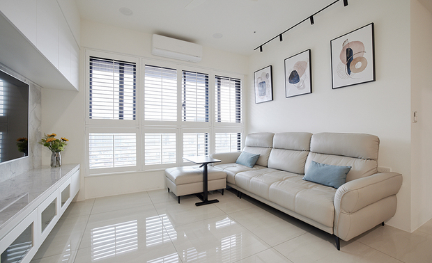 客厅
Living Room

客厅窗户前方装设白色木百叶帘，随需求引入自然光线进驻室内，并修饰黑色铝窗框的厚重感，而下方不可开启的设计，则能兼顾孩童玩耍时的安全。沙发配合周围色调，以大面积的浅色调营造柔和温馨感，搭配深色边几进行点缀，平衡色彩的视觉重量。

The living room boasts a captivating feature - a white wooden blind delicately gracing the windows. It effortlessly welcomes the gentle caress of natural light, artfully complementing the robust black aluminum window frames. The lower section, thoughtfully designed to remain non-operable, ensures the safety of playful children. To further accentuate the serene atmosphere, the sofa harmonizes flawlessly with the surrounding color palette, enveloping the space in a soothing embrace of light tones. The addition of dark side tables serves as tasteful accents, striking a perfect equilibrium in the visual composition of colors.
