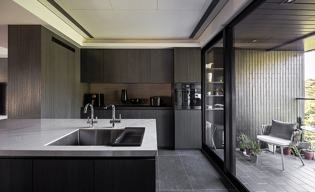 厨房
The kitchen
厨房中央设有吧台,满足简便的茶饮需求,并于侧边镂空作展示功能,减少庞大量体的厚重感;其馀的机电和柜体,则分别靠牆面两侧摆放,呈现整齐开放的视野,让落地窗外的山景进驻公领域,与其对面繁华的城市街景相映成趣。
Set an island in the center of the kitchen to meet the needs of light meals, and space out a side to result in the display function, as well as to reduce the bulky sensation of the massive setting. The electric household appliances and storage cabinets are respectively set on both sides of the wall to bring about a concise and open pattern. The natural outdoor landscape excellently introduces from the French windows and cast significant contrast to the bustling city street scene opposite.