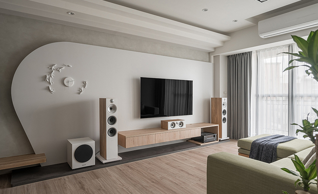 客厅
Living room

电视牆採用彷清水模材质的灰色艺术涂料及白色冷烤漆，在大片木质的衬托下，更显清朗气质，兼具美感及方便清洁之效用。因屋主希望跳脱传统的方正尺度，因此我们搭配牆面上的金鱼时钟弧度，在收尾时做弧形曲线收边，相互呼应亦彰显聚财象徵。天花板的叠加线条，层次错落，搭配自然光及室内光源，形成光影流动，明暗有致。

We exploit aesthetic gray faux fair-faced concrete coating and easy-cleaned chill white baking finish to set the TV wall, which adds refreshing features to an otherwise wooden layout. As the homeowner hopes to convert the traditional square shape, we skillfully trim an arc ending to pair with the goldfish-shaped wall clock that symbolizes wealth gathering. The natural light and indoor illuminations reflect on the crown moldings of the ceiling, brilliantly performing vivid light and shadow.
