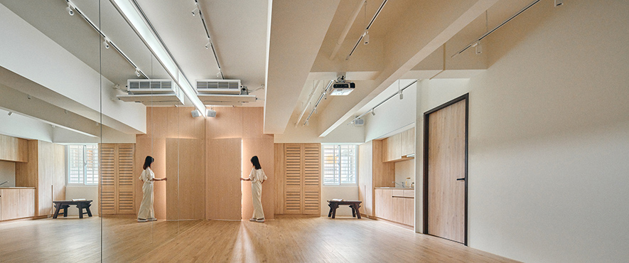 （图）八宝空间美学作品，复合式商空《茶禅》售茶处后方为现代风格的有氧教室。

复合式经营 衔接风格

除了《柚子花花》，复合式餐饮作为近年的趋势，八宝空间美学也有另一件结合有氧教室和茶行的商空作品《茶禅》，「这是一件相当有趣的作品，它在设计后期才转为复合式商空。」团队笑着分享，业主是一位父亲，原想为女儿开设舞蹈教室而委託他们，后来却因为种种巧合，让自己和儿子经营的售茶业一齐进驻，「女儿想从小规模开始经营，累积足够经验后再扩大，所以尚未用到的空间就让父子开业。」

面对截然不同的两项行业，八宝空间美学决定先找到两者的共通点，「我们后来想到运动完需补充水分，就依据父子各自擅长的茶品，做了两组试喝的茶桌区。」如此，在父亲服务喜爱传统冲泡茶的客人时，儿子也可以提供创意手摇茶饮供年轻人选择，再配合有氧教室学员的专属优惠，达成三赢的局面，「室内设计方面，我们透过简化元素，去调和运动教室的现代简约和茶行的中式风格，例如降低茶馆的木色深度、凋花门窗的繁复度，让场域能更好地衔接。」
