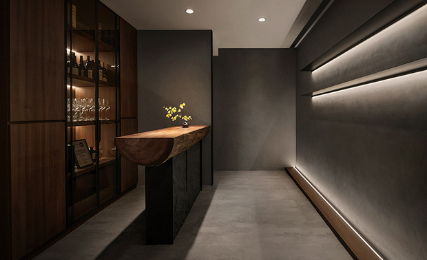 
柜檯
The Reception Counter

入门即见的素雅灰牆搭佐灯光与金属层板，以极简姿态呈现细腻的表面纹理，令顾客沉淀纷扰的思绪，一旁的柜檯面选用剖半原木，兼顾实用性和装饰性，传递自然风情。

The simple and classy gray walls, accented with lighting and metal panels, greet the guests at the entrance with a refined surface texture that calms the mind. The adjacent reception counter is crafted from split logs that blend practicality and aesthetics seamlessly, exuding a natural charm.
