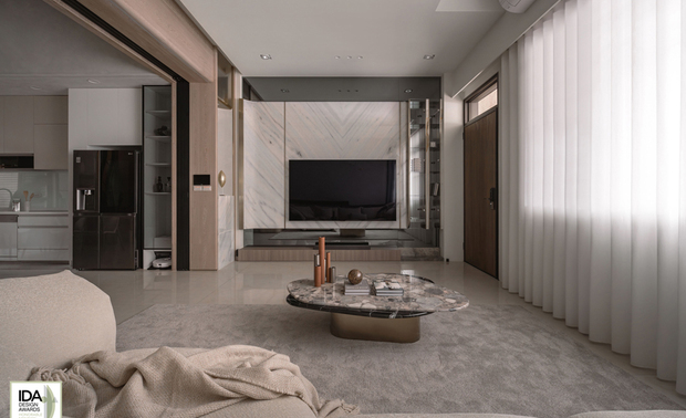 ▲客厅以香槟金髮丝纹镀钛饰条串连，与灯饰的金光呼应，灰镜电视牆收尾，打造如度假饭店般精緻场域，将屋主对悠閒优雅的生活想像精准具现。
