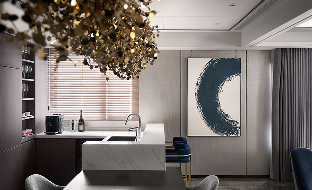 ▲餐厨区餐桌连结白色石纹吧台，提供轻食准备兼休閒的理想场所。一幅蓝灰渐层的抽象画作与另一侧的圆弧水墨画，为该区注入艺术气息，同时再次呼应上空四颗吊灯，强调「圆满」之意。
