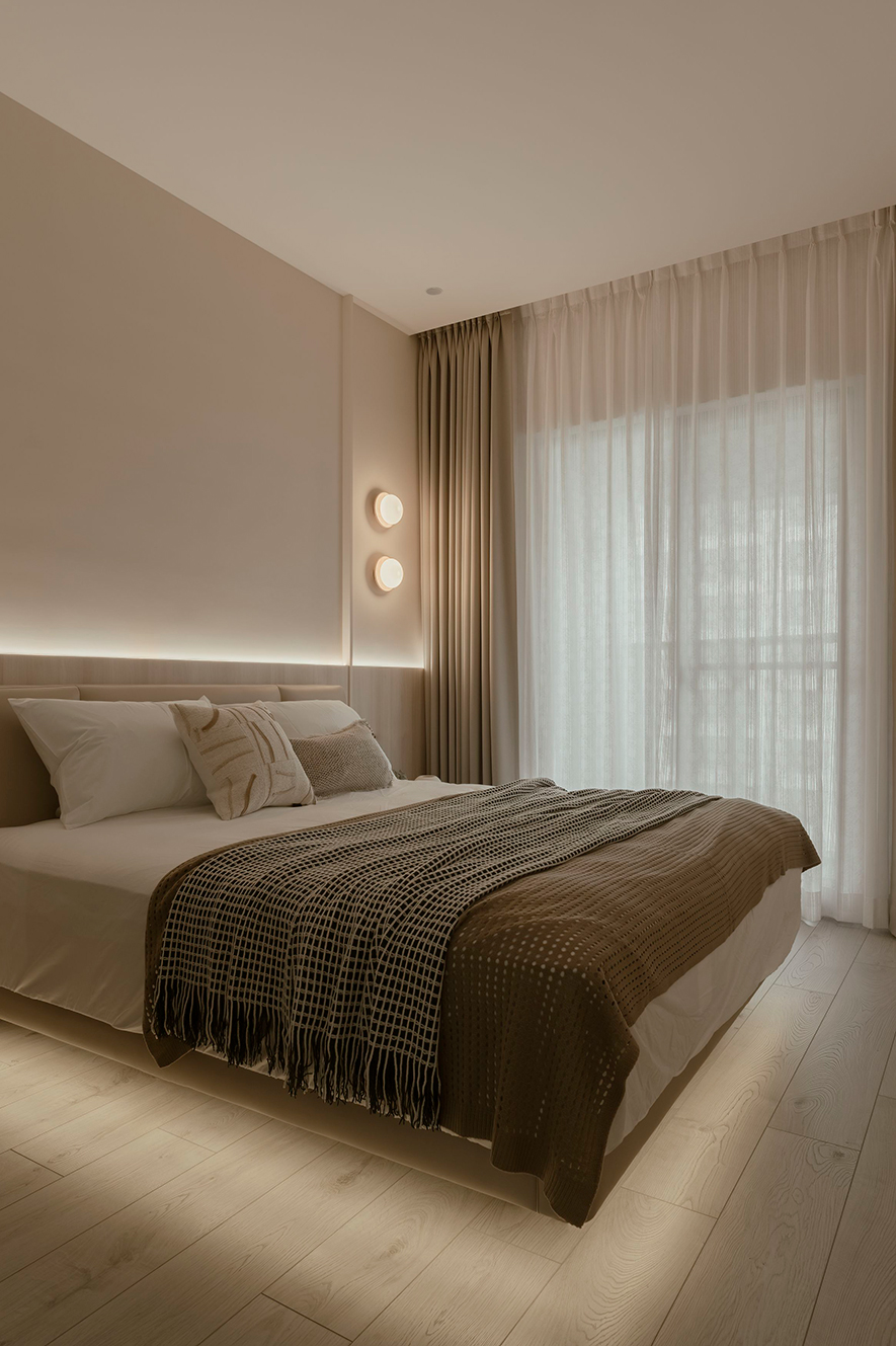
主卧——暖灯高悬 遍洒一室怡然惬情

呼应公领域的浅雅语彙，主卧舖陈柔米、澹木基底，辅以床架下、床背板后方特别藏设的间接灯光，令漫流光影染出色阶间的暖煦温度，佐搭床头上下并列的两盏圆润壁灯，如明月缓缓攀升，营造诗意缭绕的写意氛围。整体在素朴简约中融入温情，使卧房回归可沉心舒展的休憩空间。
