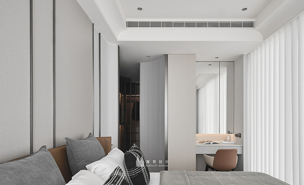
主卧——浅灰基调交织垂直线条 纯粹色域中的宁静归处

推开主卧房门，一道细密排列的垂直格栅隔屏划出柔和分界，其圆弧转折为私密领域营造一份恰到好处的含蓄感。绕过隔屏，进入以浅灰色调铺叙的寝居空间，床头背牆简约框线奠定素雅底蕴，配合对向大片落地窗透过白色窗帘，洒落柔和日光，让主卧在不同时刻呈现丰富流光变化；窗边梳妆台立面同样採用纵向沟缝，辉映入口元素，于一脉相承的线条中见设计之匠心，晨起时分，在自然光的轻抚下整理仪容，便是一日美好的开端。
