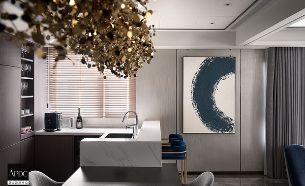 ▲餐厨区餐桌连结白色石纹吧台，提供轻食准备兼休閒的理想场所。一幅蓝灰渐层的抽象画作与另一侧的圆弧水墨画，为该区注入艺术气息，同时再次呼应上空四颗吊灯，强调「圆满」之意。
