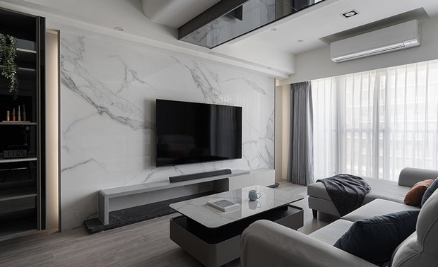 
客厅——光隐曲梁 轻绘内敛格调

客厅以纯淨的白色石纹电视牆为视觉焦点，其自然肌理与旁侧深色木质展示柜形成明暗对比，开放格架层层递进，错落陈列的精选物件为立面增添丰富层次；而天花板运用弧形包覆搭配镜面反射，将原本横亘的大梁化为优雅曲线，隐藏式灯带勾勒出层次分明的光影轮廓，与落地窗透入的自然日光交相呼应，为灰色布质沙发及黑白茶几围塑的会客区域凝结温润气韵，酝酿沉稳内敛却不失温度的居家氛围。
