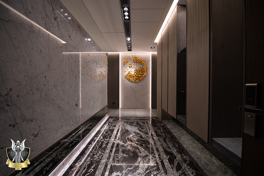 ▲玄关地坪选用泼墨山水、金色山脉二种石材，透过石纹肌理清楚框划出场域，左侧立面共用电视牆量体，其倒L型的镂空设计不仅营造轻盈悬浮感，上方延伸的灯带也达到引导观者入室的效果。
