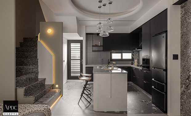 ▲与厨房黑色门板的俐落线条相互呼应，烹饪区选用浅灰色长型铁道砖搭配黑色填缝剂，刻意凸显砖材轮廓，营造精緻质感；中央的吧檯以圆润线条感，柔和融入整体空间语境，既是料理工作檯，更作为家人情感交流的枢纽，亲子互动在开放格局中自然发生。
