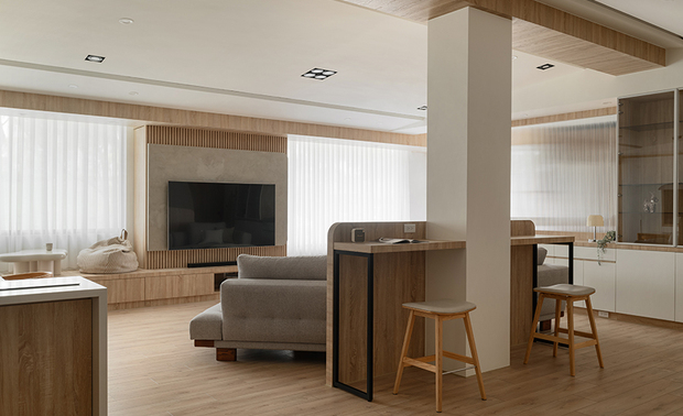 
客厅——素淨雅韵 开阔怡心

客厅灰色织物沙发低调沉稳，搭配圆形桌面的木质底座茶几，营造质朴而不失雅緻的会客场所；沙发半高背牆巧妙融入工作桌功能，既是空间的分界，亦为居者于开放格局中寻得专注一隅。对向大片落地窗将户外绿意尽收眼底，阳光透过纱帘的过滤，化作柔和的光晕洒落；而窗边长型卧榻以盈润木调材质包覆，素雅软垫相衬，恰似文人雅士的「观景榻」，供人品茗观云、静思冥想。整体细腻回应着生活的多重需求，在开阔无碍中保有各自的场域感，让日常的每个片刻都能找到最适切的安放之处。
