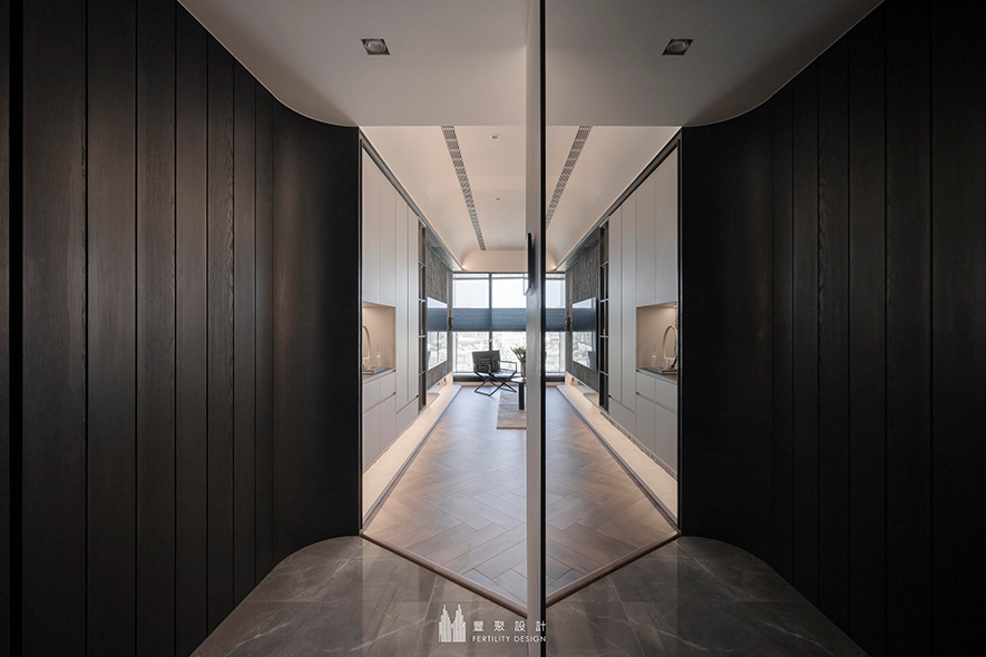 
玄关——暗色木皮×落地镜面 打造视觉延展的沉心入门场所

玄关立面拼贴层递有序的深色木皮，让温润宁静感迎接归者，彻底平復在外繁忙一日的浮躁心境；对侧，顶天立地的落地镜牵引光线，将所见之处的景深悄然拉长，而光影反射间的异材细节烘托，展露神秘高雅气质，铺陈一段安定细腻的入室前奏，同时倒映木质的暗影与公区的明亮，使色彩对比展开渐次轻盈的明暗层次，进一步强化屋内空间的敞亮清透。
