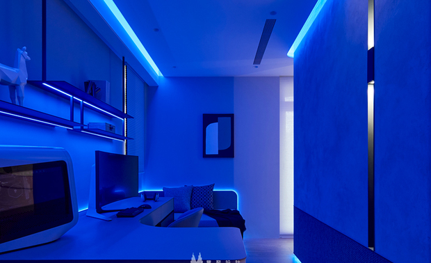 
书房——电竞幻想 科技与情感的沉浸空间

如穿越时空界线，踏入另一个次元般，眼前是一片深邃的蓝色光海，像潜入深海的宁静，又像漂浮星空的辽阔。RGB变色灯条让光带如电流般环绕天花、牆面与层架，四周白色书桌与陈列架在流动光影映照下，呈现超现实的梦幻质感，彷彿置身顶级电竞馆的绚丽场景。无论是深夜工作的专注时刻，或是放鬆身心的游戏时光，此处都以最包容的姿态接纳每一种状态，在独特的电光异境中，让每一场的投入都成为心灵的充电时刻。
