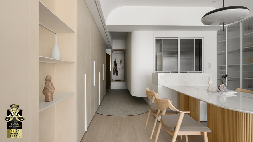 ▲玄关设木质圆框穿鞋椅兼具挂衣功能，搭配一旁圆弧茶镜营造简约的廊道端景；地坪採大面板水磨石砖呈现无缝质感，与室内木地板交界处以弧形镀钛铁件收边，呼应天花圆弧设计，为空间增添精緻亮点。
