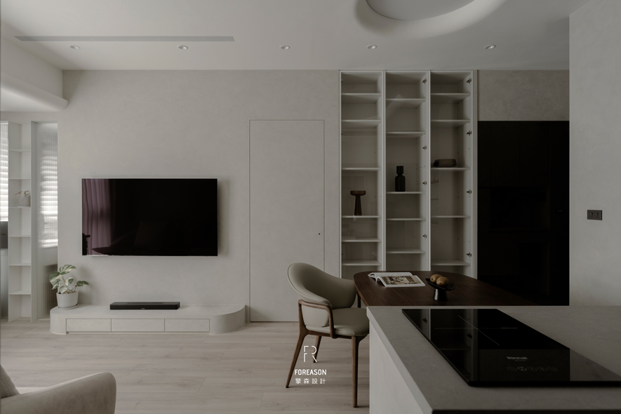 
客厅——淨白场域 围塑心灵绿洲

客厅选配纯白为基调，浅色木纹铺陈温润肌理。正前方电视牆採极简手法，悬挂式电视搭配白色矮柜延伸俐落轮廓，置于柜上的绿植点缀生机，让热爱植栽的屋主能在日常浇灌中，看见绿意随四季流转的灵动生命力。两侧高耸的白色展示柜成为空间端景，长虹玻璃门片如水波般折射光线，开放式层架陈列旅行带回的纪念品及珍藏的艺术品，记录回忆中所有的点滴美好。整体在素淨中蕴含细緻感受，构筑令人心神沉静、能真正放鬆生活的场景。
