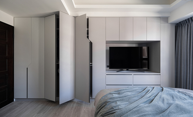 
主卧——清雅蓝韵 织就恬淡梦境

步入主卧，浅蓝色调如清晨薄雾般温柔包覆床头背牆，隐藏门片的设计将浴室入口悄然融入其中，维持立面的纯粹完整，与不对称的几何切割的纯白储物柜门片展开清新对话，斜角线条的灵动设计打破传统方正格局的同时保有简洁美感，共同围塑出简约纯淨的氛围；天壁内嵌的柔和照明如月光般均匀洒落灰色织物床组，增添质朴气息，窗畔垂落的深灰窗帘则为这方天地融入稳重感，在这以轻柔色调为主的私密领域中，交织和煦的安眠情境，为居者实现梦寐以求的恬淡卧房。
