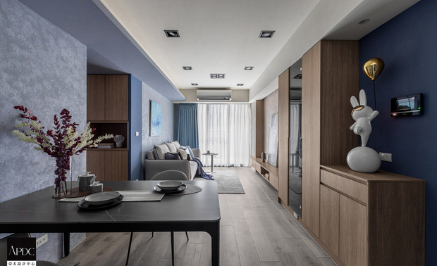 ▲餐厅设置飘逸时尚气息的黑色圆角餐桌及灰色餐椅，和厨房内部的简约黑白相得益彰，于细緻灰蓝涂料质感中酝酿洗鍊雅痞风；客厅电视牆和沙发背牆以大地色系的素朴与天空般的清爽蓝色渐层，仿拟业主美好回忆中，飞机起降时的每刻优美风景，伴其度过假期的慵懒小酌的閒适时光。
