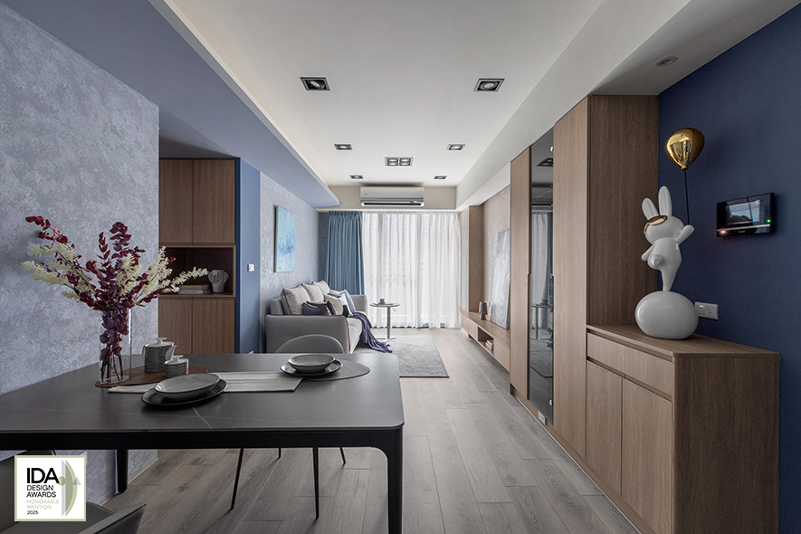 ▲餐厅设置飘逸时尚气息的黑色圆角餐桌及灰色餐椅，和厨房内部的简约黑白相得益彰，于细緻灰蓝涂料质感中酝酿洗鍊雅痞风；客厅电视牆和沙发背牆以大地色系的素朴与天空般的清爽蓝色渐层，仿拟业主美好回忆中，飞机起降时的每刻优美风景，伴其度过假期的慵懒小酌的閒适时光。
