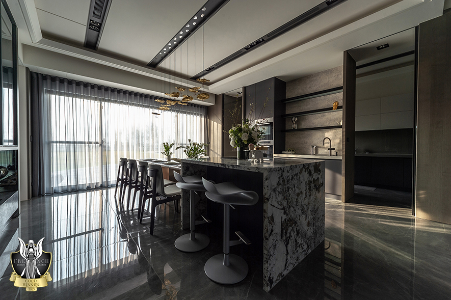 ▲客餐厅交界处规划一道茶镜水磨砂玻璃拱门，古铜色金属光泽质感酿出雍雅大气艺韵之馀，区划两处功能场所，场域中央置入衔接一座中岛的餐桌，打造可容纳至多十人的宽敞交谊空间。
