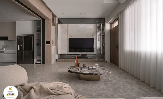 ▲客厅以香槟金髮丝纹镀钛饰条串连，与灯饰的金光呼应，灰镜电视牆收尾，打造如度假饭店般精緻场域，将屋主对悠閒优雅的生活想像精准具现。
