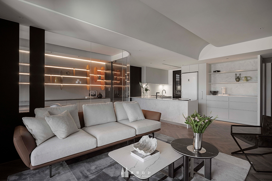 
客餐厅──巧运流弧柔化建物刚硬线条 围塑优美宽敞的公共空间

公区天壁藉数笔柔弧牵开建物原有的硬朗轮廓，彷彿在方正框架之中引入一缕流动的风，配合顺应屋主轻食习惯而捨弃制式餐桌的安排，为空间捎来清新舒朗的开阔呼吸感。餐厨区内，L型厨房、餐边柜与冰箱形成井然的黄金三角，让取物、洗涤、备餐的日常自然而从容，提升生活便捷性；一旁的客厅则以手工拼贴的电视石牆为焦点，每道凹凸肌理、石纹痕迹，皆宛如刻写光影的诗行，随晨暮交替变幻不同的字词音律，陪伴居者在停留歇憩的时光裡，慢慢沉入属于家的绝美情境。
