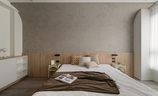 
主卧——圆融静谧 梦境归处

延续一室素淨的木质调性，主卧以轻盈曲线开展空间序章，巧妙化横樑的突兀感为优雅的曲面语彙。天然的木纹床头板如大地般沉稳厚实，衬托灰白色调牆面，造就宁静致远的休憩氛围。两侧的圆弧造型床头柜，以几何线条勾勒出柔美轮廓，上方搭配黑色壁灯，更显静雅沉稳，编织出一方安适的梦境之所，伴随居者夜夜好眠。
