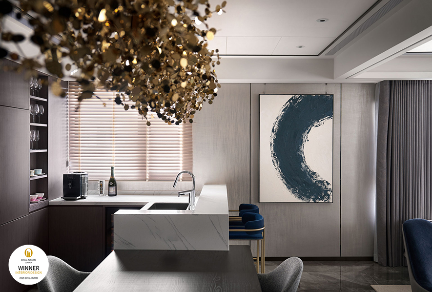 ▲餐厨区餐桌连结白色石纹吧台，提供轻食准备兼休閒的理想场所。一幅蓝灰渐层的抽象画作与另一侧的圆弧水墨画，为该区注入艺术气息，同时再次呼应上空四颗吊灯，强调「圆满」之意。
